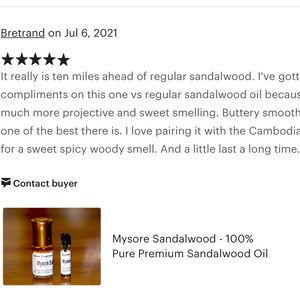 Op de afbeelding: Twee kleine flesjes Mysore Sandelhout 100% Pure Premium Sandelhout Olie. De flesjes zijn van helder glas met gouden dopjes en etiketten. De flesjes staan op een houten oppervlak.