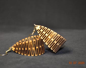 May include: A pair of dangle earrings crafted from light-colored wood, featuring a repeating geometric cutout pattern with dark, burnt-edge detailing. Each earring is suspended from a gold-toned metal hook, showcasing a curved, elongated shape.