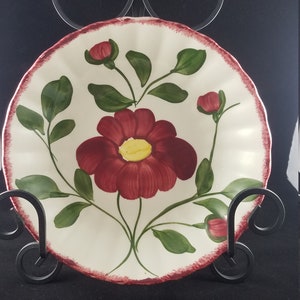 May include: A white ceramic plate with a red and green floral design. The plate has a scalloped edge and a red rim.