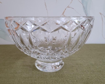 May include: A clear crystal bowl with a cut glass design and a pedestal base. The bowl is sitting on a green fabric surface.
