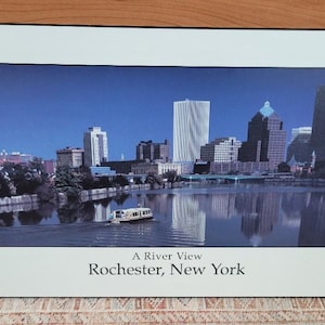 May include: A framed photograph of a city skyline with a river in the foreground. The city is Rochester, New York. The text "A River View" and "Rochester, New York" is printed below the image.