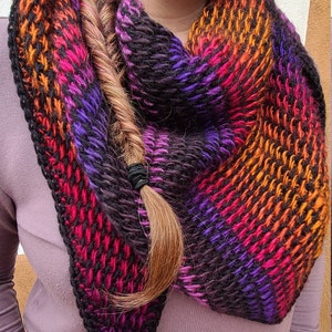 Puede incluir: Una bufanda de punto colorida con rayas negras, naranjas, rojas y moradas.