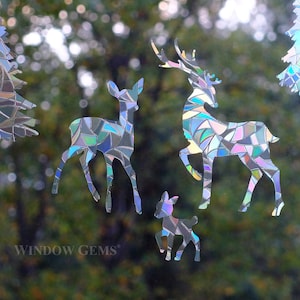 May include: A set of iridescent window clings featuring a deer family and pine trees. The clings are made of a mosaic-like material that reflects light.