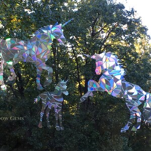 May include: Three iridescent unicorn window clings, one large, one medium, and one small, against a green leafy background. The unicorns are made of iridescent mosaic pieces.