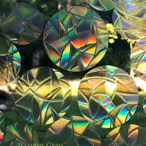 May include: A sheet of iridescent window film with a geometric pattern of circles. Each circle has a stained glass design with a rainbow of colors. The film is designed to add privacy and style to windows.