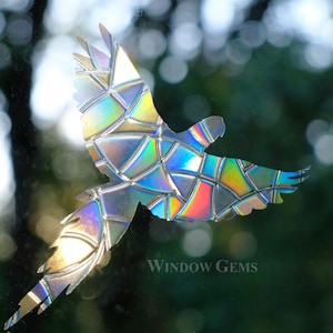 May include: A colorful iridescent bird silhouette made from mosaic glass pieces. The bird is in flight with its wings spread wide. The background is blurred and out of focus.