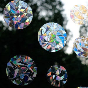 May include: A set of six iridescent window clings in a stained glass pattern. The clings are round and feature a variety of colors, including blue, green, purple, and gold. The clings are designed to add a decorative touch to any window.