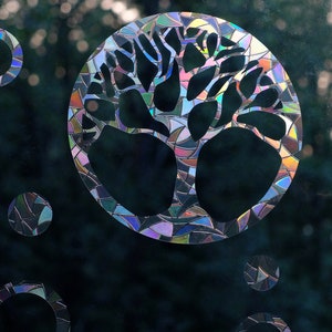 May include: A stained glass window decal featuring a tree with a circular design. The decal has a rainbow iridescent finish and is surrounded by smaller circular designs.