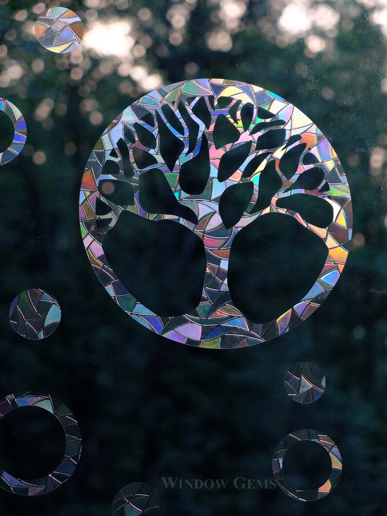 May include: A stained glass window decal featuring a tree with a circular design. The decal has a rainbow iridescent finish and is surrounded by smaller circular designs.