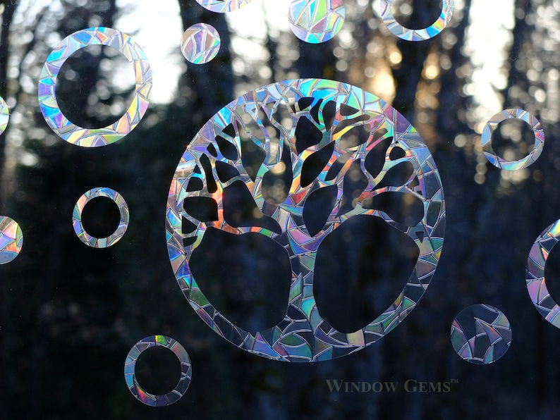 May include: A holographic window cling featuring a tree of life design with a circular frame. The cling is made up of iridescent mosaic pieces and is surrounded by smaller circular clings.
