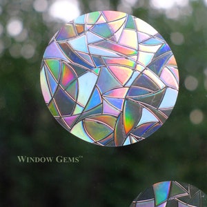 May include: Two iridescent window clings in the shape of circles. The larger circle has a geometric design with a mix of blue, pink, and purple hues. The smaller circle has a similar design with black, purple, and blue hues. The text "WINDOW GEMS&trade;" is visible at the bottom of the image.