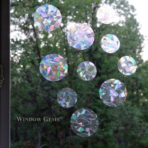 May include: A set of iridescent window clings in the shape of circles. The clings are made of a clear material with a rainbow-like pattern. The clings are arranged in a random pattern on a window. The text "WINDOW GEMS&trade;" is visible in the bottom left corner of the image.