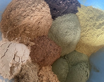Può includere: Primo piano di varie erbe e polveri essiccate in una ciotola blu. L'assortimento comprende sfumature di marrone, verde e beige, con consistenze che vanno da polveri sottili a materiali più grossolani e fibrosi. L'immagine suggerisce un focus sugli ingredienti naturali.