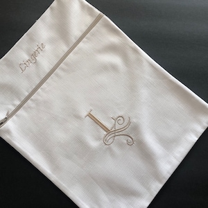 Peut inclure: Un sac de rangement en tissu blanc avec une fermeture éclair, orné du mot brodé Lingerie et d'une grande lettre I décorative en fil marron clair. Le sac présente un tissage texturé et une forme rectangulaire pour organiser vos affaires.