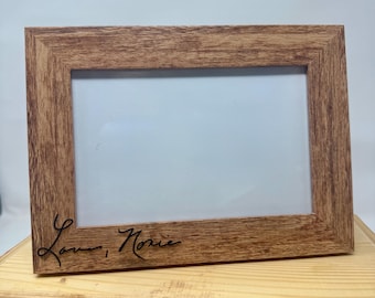 Op de afbeelding: Een rechthoekige fotolijst met een lichtbruine houtnerfafwerking. De lijst is voorzien van een witte inzet en de zwarte cursieve tekst "Love, Nonie" gegraveerd in de linkerbenedenhoek van de houten rand, wat zorgt voor een heldere en eenvoudige uitstraling.