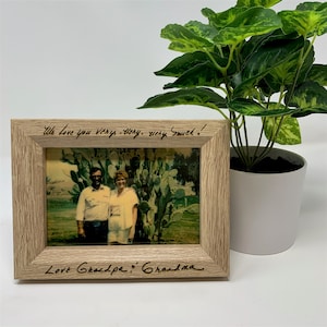 May include: A wooden picture frame with a photo of an older couple standing in front of a cactus. The frame has a handwritten message that says "We love you very very very much! Love Grandpa & Grandma".