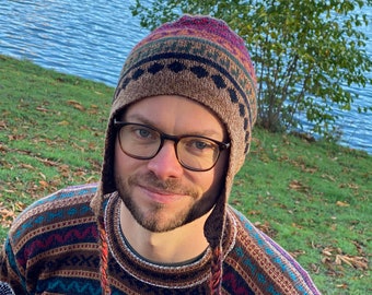 Può includere: Un uomo che indossa un maglione di lana marrone e multicolore con un cappello di lana abbinato. Il maglione ha un motivo geometrico e il cappello ha un pon pon.