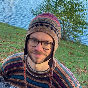 May include: A man wearing a brown and multi-colored knitted sweater with a matching knitted hat. The sweater has a geometric pattern and the hat has a tassel.