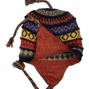 The alpaca wool earflap hat laid flat, displaying its colorful design and tassel details.