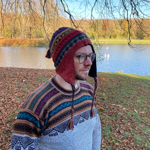 Another side view of the model with the hat, highlighting the pattern, earflaps, and braided tassels near a lake.