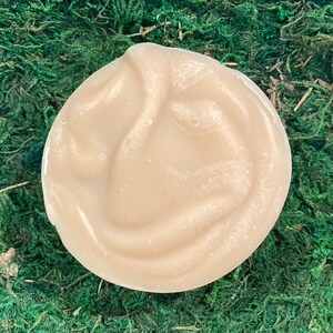 Op de afbeelding: Een close-up van een lichtbeige, romige, gladde en licht glimmende zeep. De zeep is rond en heeft een swirl-patroon.
