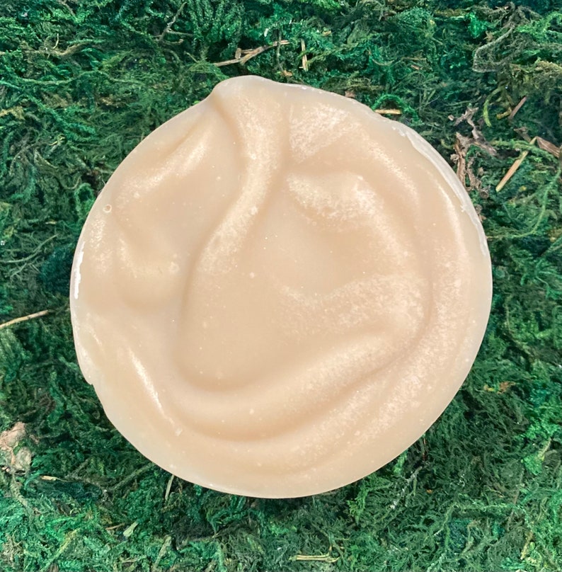 Op de afbeelding: Een close-up van een lichtbeige, romige, gladde en licht glimmende zeep. De zeep is rond en heeft een swirl-patroon.