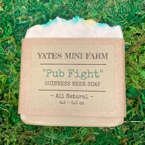 May include: A bar of Guinness beer soap from Yates Mini Farm, wrapped in brown paper. The label reads "Pub Fight" and "Guinness Beer Soap". The soap is white with blue and yellow accents and weighs 4.5-5.0 oz.
