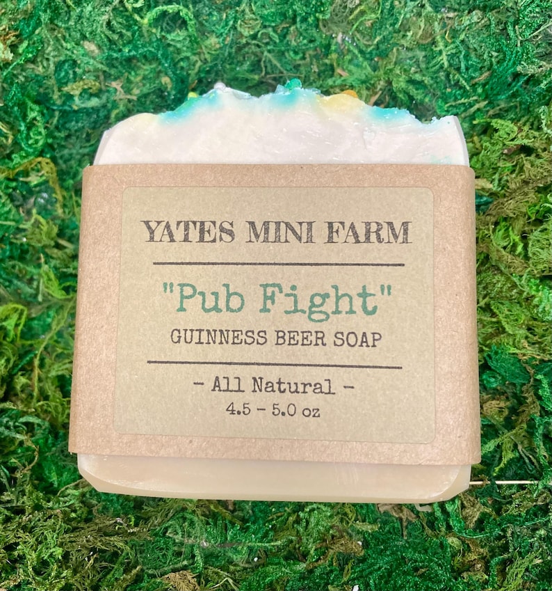 May include: A bar of Guinness beer soap from Yates Mini Farm, wrapped in brown paper. The label reads "Pub Fight" and "Guinness Beer Soap". The soap is white with blue and yellow accents and weighs 4.5-5.0 oz.