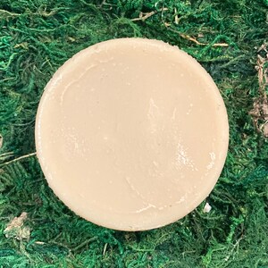 Op de afbeelding: Een ronde, lichtbruine zeep. De zeep ligt op een bed van groen mos.