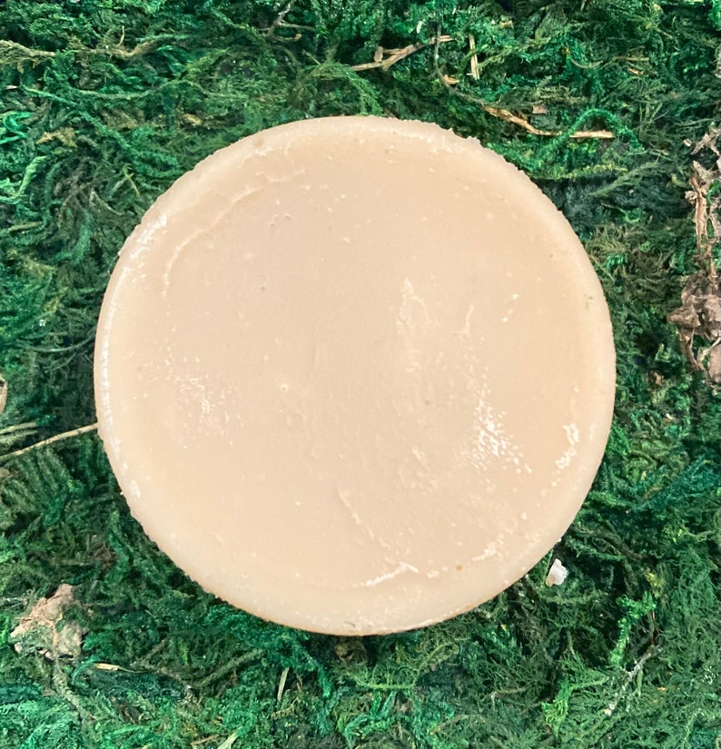 Op de afbeelding: Een ronde, lichtbruine zeep. De zeep ligt op een bed van groen mos.