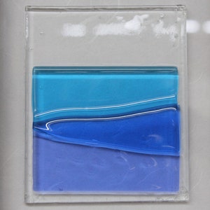 May include: A framed piece of art with layered blue glass. The glass is layered in shades of blue, from light to dark, and the layers are slightly wavy.
