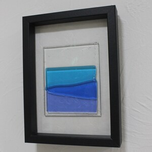 May include: A framed piece of art featuring a layered glass design with shades of blue and purple.