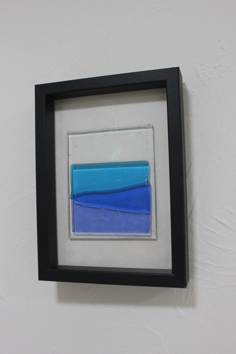 May include: A framed piece of art featuring a layered glass design with shades of blue and purple.