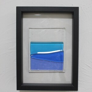 May include: A framed piece of art featuring a layered glass design with blue and purple hues. The glass is set in a black frame.