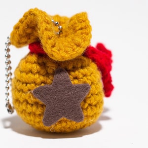 May include: A crocheted yellow bag with a red ribbon and a brown felt star. The bag has a silver chain attached to it.