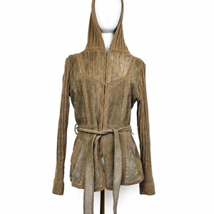 May include: A tan hooded jacket featuring a central zipper closure and a matching tie belt at the waist. The garment is constructed with a combination of suede-like panels and ribbed knit sleeves and hood, accented with visible decorative stitching.