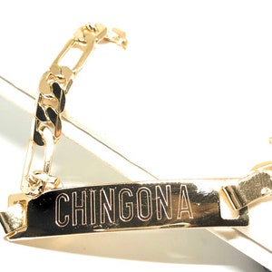 May include: Gold chain bracelet with a rectangular tag that says "CHINGONA".