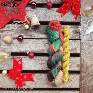 Puede incluir: Dos ovillos de hilo, uno verde, rojo y marrón, y otro amarillo, sobre una superficie de madera con adornos rojos y dorados y una campana.
