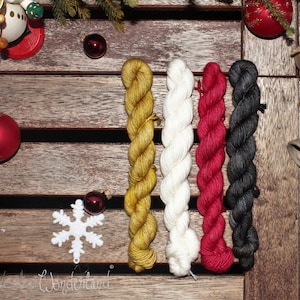 Puede incluir: Cuatro ovillos de hilo en diferentes colores: dorado, blanco, rojo y negro. El hilo está dispuesto verticalmente sobre una superficie de madera.