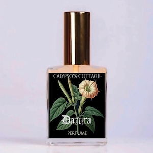 May include: A clear glass perfume bottle with a gold cap. The label features a botanical illustration of a white flower and green leaves, with the word "Datura" and the word "PERFUME" below it. The brand name "CALYPSO'S COTTAGE" is at the top.