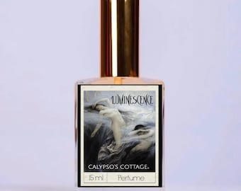 May include: A clear glass perfume bottle with a gold cap, featuring a rectangular label with the text Luminescence, Calypso's Cottage, and 15 ml Perfume. The label displays an illustration of two figures in a dark, swirling environment.