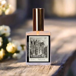 May include: A perfume bottle with a gold cap and a label featuring a black and white illustration of a city scene. The label reads "London Fog" and "15 ml Perfume". The bottle is clear, and the liquid inside is a light peach color.