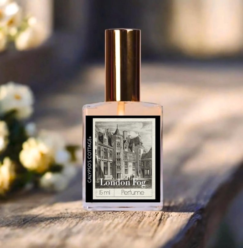 May include: A perfume bottle with a gold cap and a label featuring a black and white illustration of a city scene. The label reads "London Fog" and "15 ml Perfume". The bottle is clear, and the liquid inside is a light peach color.