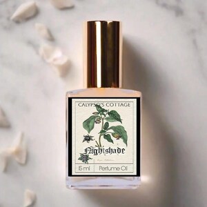 Op de afbeelding: Een parfumolie flesje met een gouden dop en een etiket met een botanische illustratie van een plant met de naam "Nightshade". Het etiket bevat ook de tekst "CALYPSO'S COTTAGE" en "15 ml Perfume Oil."