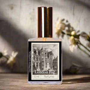 May include: A clear perfume bottle with a gold cap and a label featuring a black and white illustration of a building. The label reads "London Fog" and "Perfume". The bottle is 15 ml and is from Calypso's Cottage.