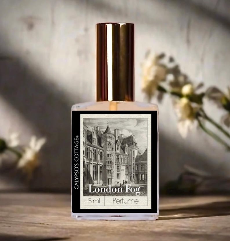 May include: A clear perfume bottle with a gold cap and a label featuring a black and white illustration of a building. The label reads "London Fog" and "Perfume". The bottle is 15 ml and is from Calypso's Cottage.