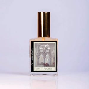 Puede incluir: Un frasco de perfume de vidrio transparente con tapa dorada. La etiqueta dice "Temple Incense" con una ilustraci&oacute;n de un edificio arqueado. La botella tambi&eacute;n tiene el texto "CALYPSO'S COTTAGE" y "5 ml Perfume".