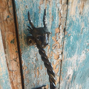 May include: Black metal dragon head door handle with a twisted metal stem. The handle is mounted on a wooden door with blue paint.