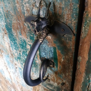May include: A black metal door handle with a dragon head design. The handle is attached to a wooden door with a distressed green paint finish.