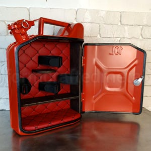 Pu&ograve; includere: Una tanica di metallo rossa trasformata in un armadietto con una porta a cerniera. L'interno presenta un rivestimento in pelle rossa trapuntata, ripiani e cinghie nere. La porta &egrave; aperta, rivelando l'interno e la scritta "JOT".